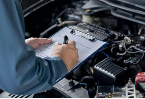 Technician completing a used car inspection checklist on a clipboard over an open engine bay
