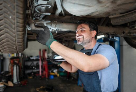 Mechanic inspecting the exhaust and undercarriage of a vehicle on a lift