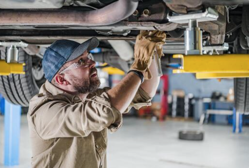 Mechanic performing an undercarriage inspection on a vehicle raised on a shop lift