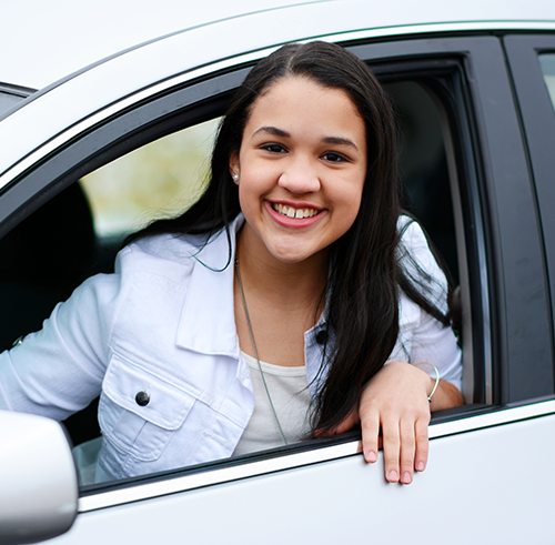 Brunette woman in white car and clothes smiling